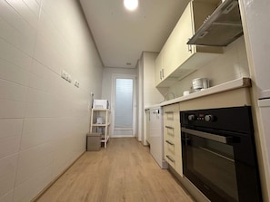 Une cuisine étroite avec des meubles blancs, un four à micro-ondes et une cuisinière.