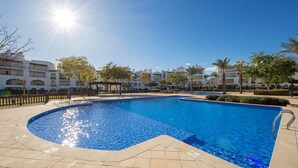 A swimming pool with a sunlit sky, surrounded by buildings and palm trees.
