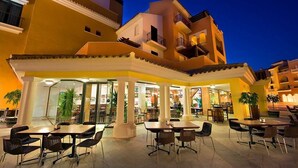 An outdoor cafe area with tables and chairs, surrounded by yellow buildings with balconies.