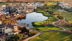 A golf course with a water hazard, surrounded by residential buildings and palm trees.