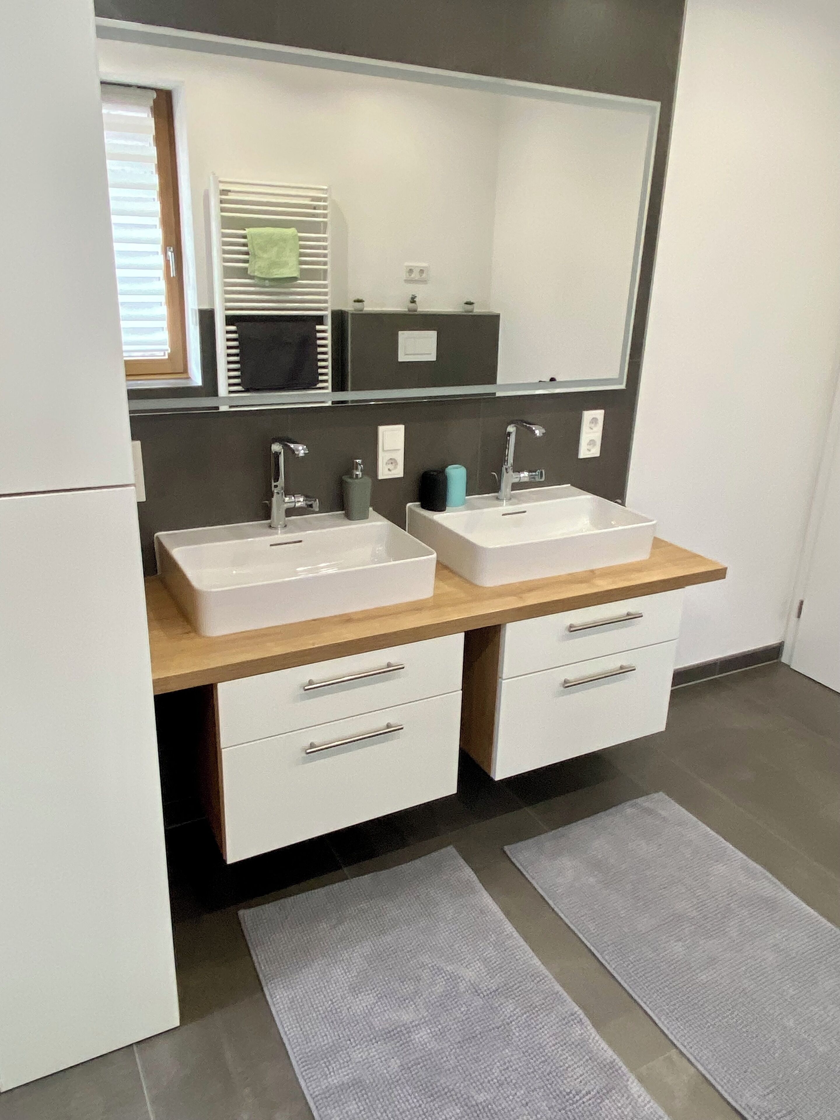 A modern bathroom with two sinks, a mirror, and a window with blinds.