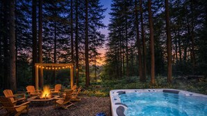 Ein Whirlpool, umgeben von hohen Bäumen, eine Holzterrasse mit Stühlen und Lichterketten.