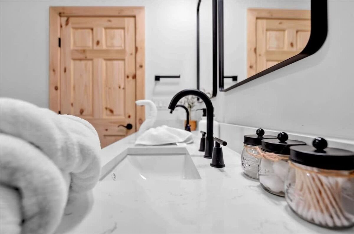 A bathroom with a white sink, black faucet, and a mirror. There are jars with lids and a towel on the counter.