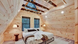 Ein gemütliches Schlafzimmer im Dachgeschoss mit Holzwänden, einem Bett, zwei Fenstern und Lichterketten.
