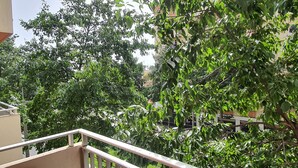 A balcony with a view of dense green trees and a building in the background.