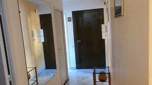 A hallway with a marble floor, a mirror, a door, and a small table with a vase.