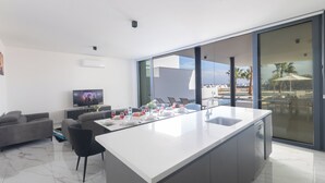 Uma cozinha moderna com uma ilha central, uma área de refeições com cadeiras, um sofá e uma TV ao fundo.