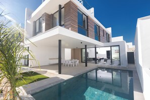 Une maison moderne à deux étages, dotée d’une piscine, d’un espace de détente extérieur et d’une pelouse bien entretenue.