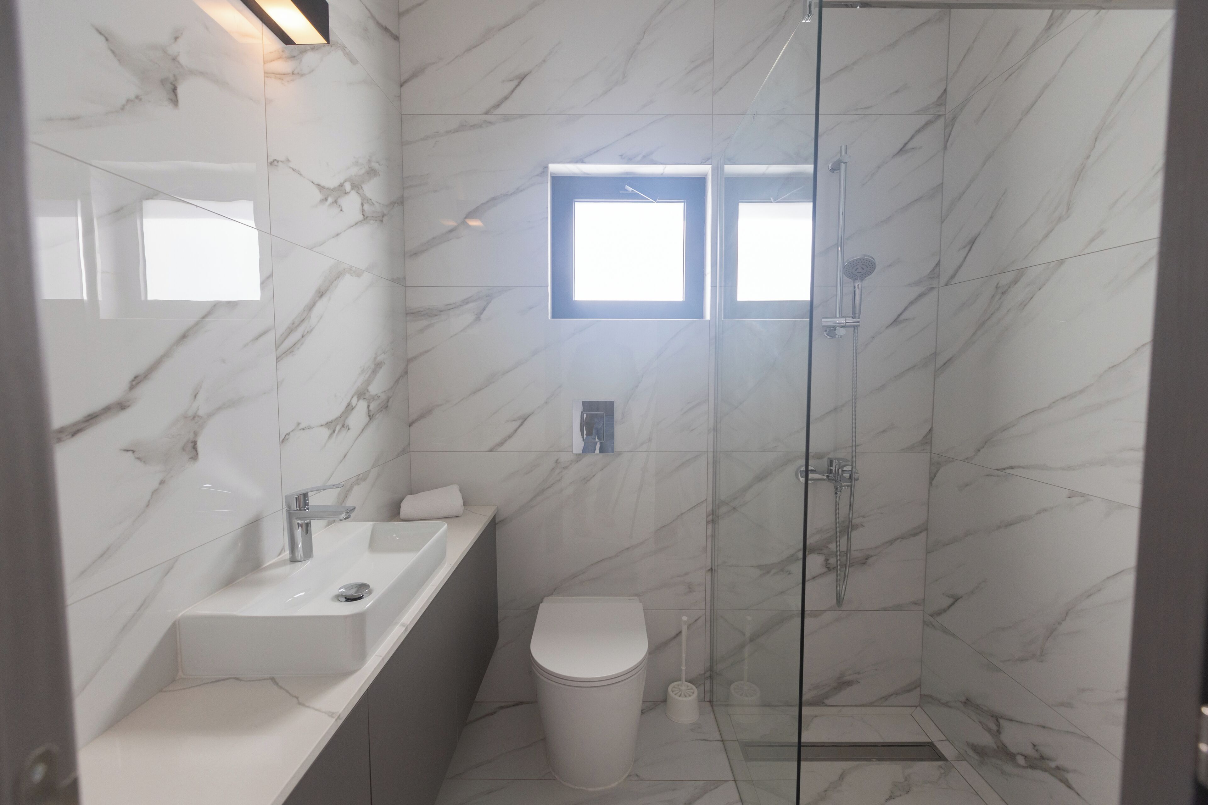 A bathroom with a marble wall, a sink, a toilet, and a glass-enclosed shower area.