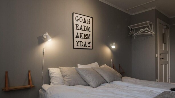 Un dormitorio con una cama, dos lámparas de noche, una lámpara de pared con texto y una puerta con perchero.