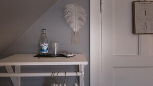 Una mesa blanca con una botella de agua LOKA, un vaso y un objeto pequeño. Una decoración de pluma blanca cuelga en la pared.
