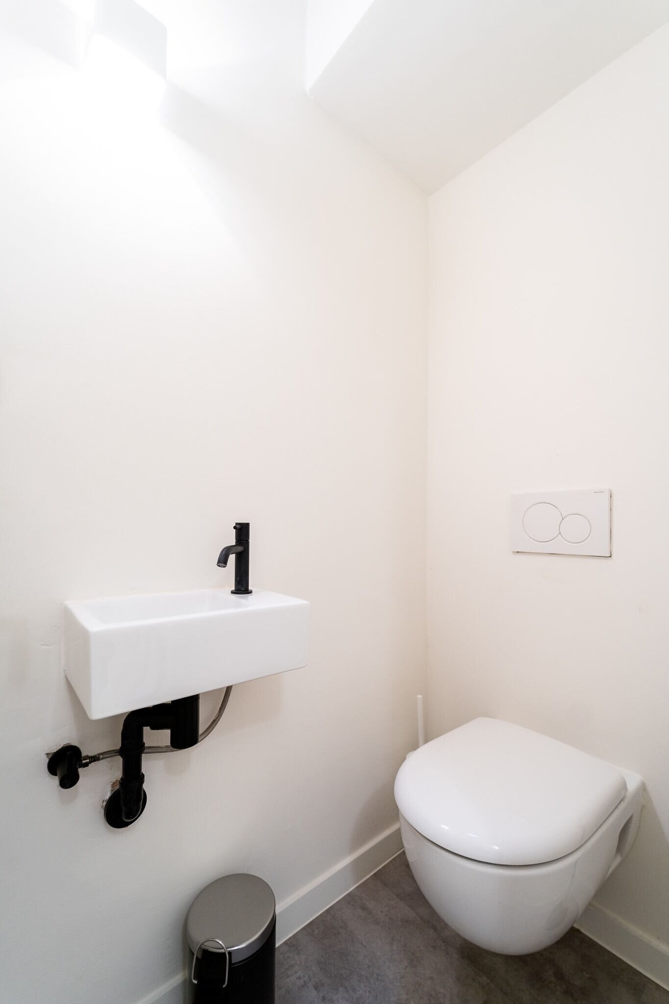 Ein kleines, weißes Badezimmer mit Waschbecken, Toilette und Mülleimer.