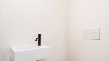 Ein kleines, weißes Badezimmer mit Waschbecken, Toilette und Mülleimer.