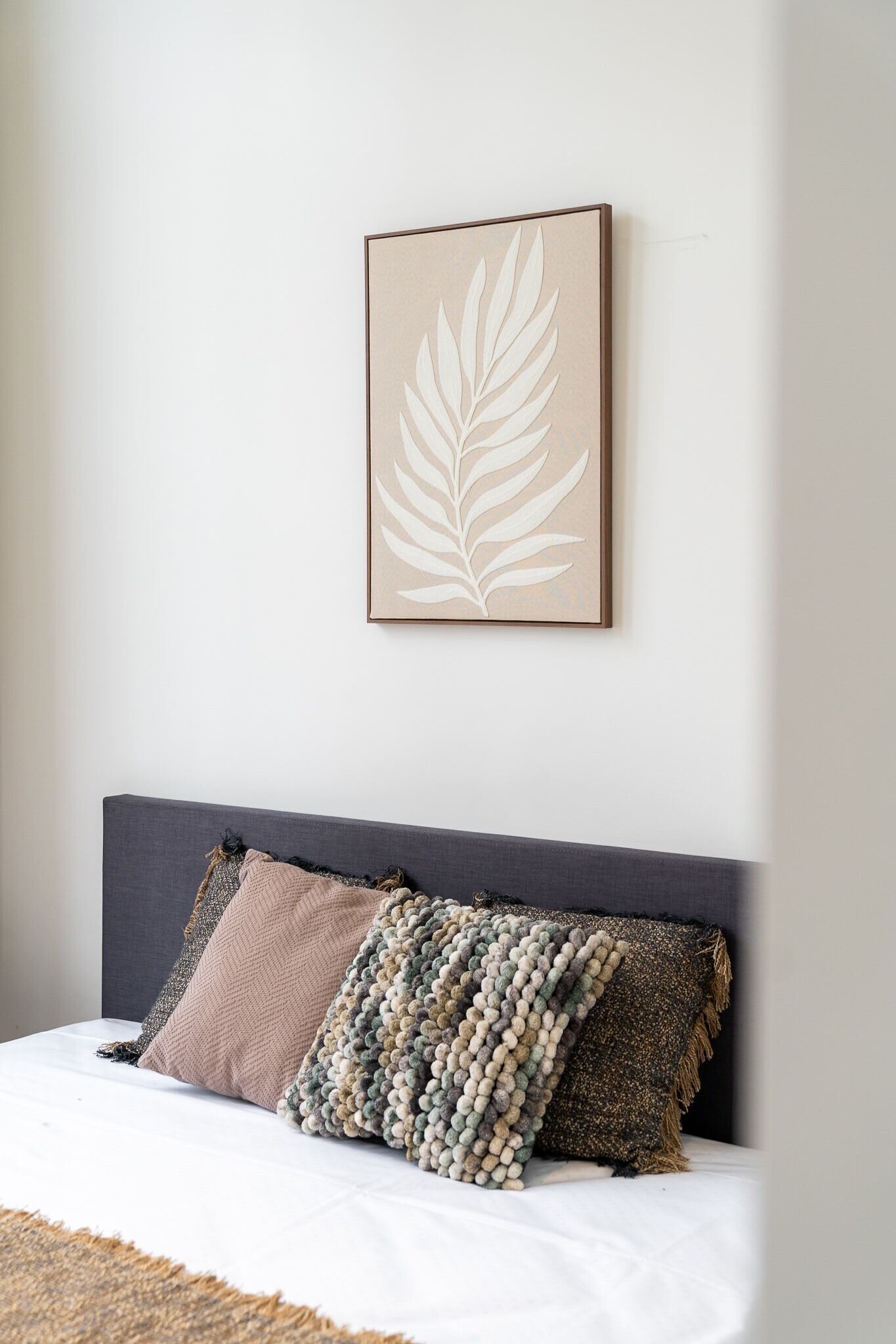Una camera da letto con un letto, una testiera e un'opera d'arte a forma di foglia appesa al muro.