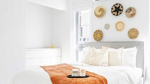 A modern bedroom with a large bed, a bedside table, a nightstand, and a window. - AQUA Casa A8 · Private & FUN 3 BR House with Pool (Dorado)