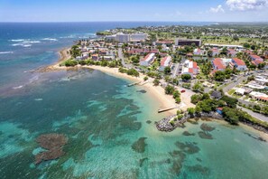 Vista aérea de un complejo turístico costero con propiedades frente a la playa, aguas cristalinas y una vista distante del océano.