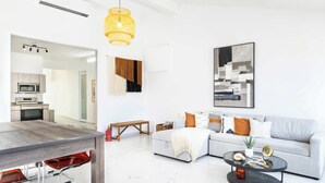 A modern living room with a dining area, a grey sofa, a coffee table, and a hanging light fixture. - AQUA Casa A8 · Private & FUN 3 BR House with Pool (Dorado)