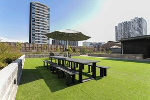 Relax in the serene outdoor patio, surrounded by lush greenery and shaded by a large umbrella.