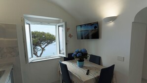 Un comedor con una mesa, sillas, una planta en maceta, un televisor y un ventanal con vista a árboles.
