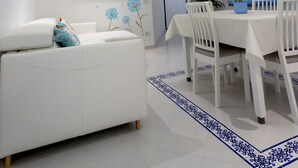 Una sala de estar moderna con un sofá blanco, una mesa de comedor con sillas, un televisor de pantalla plana y una cocina con refrigerador y armarios.