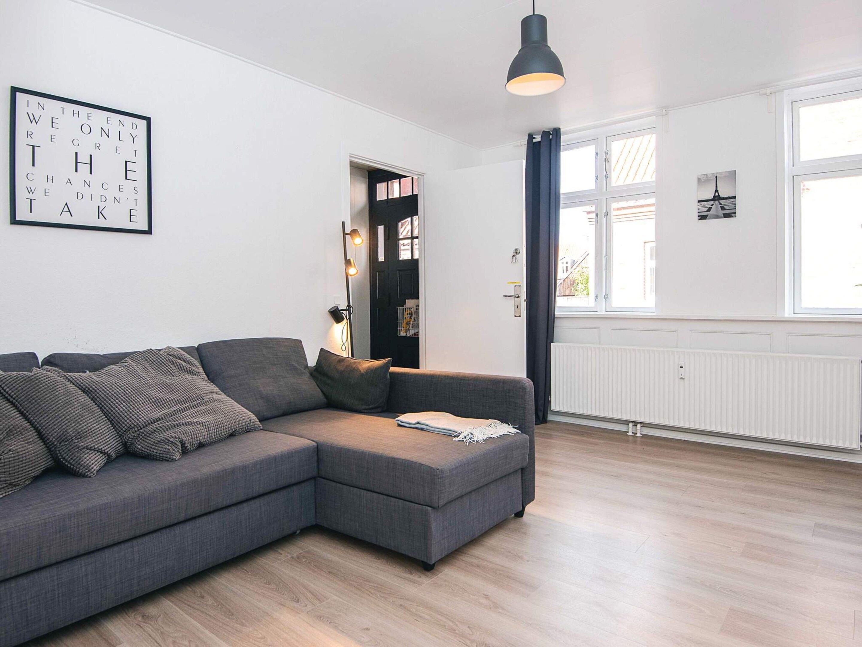A modern living room with a grey sectional sofa, a pendant light, and a framed inspirational quote on the wall.