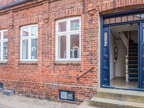 Un bâtiment en briques rouges, avec des fenêtres à encadrement blanc et une porte bleue.