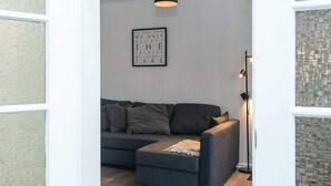 A modern living room with a grey sofa, a small ottoman, and a black pendant light. - 4 Person Holiday Home in Ringkobing (Ringkobing)