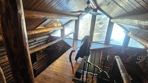 L’intérieur d’un chalet rustique, avec un plancher en bois, une table centrale et un ventilateur de plafond.