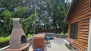 Une terrasse en bois avec un barbecue en pierre, un espace salon extérieur et une vue sur la forêt.