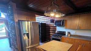 Une cuisine rustique avec des meubles en bois, un mur d’accent en pierre, un réfrigérateur en acier inoxydable, un four à micro-ondes et une table à manger en bois avec des chaises.
