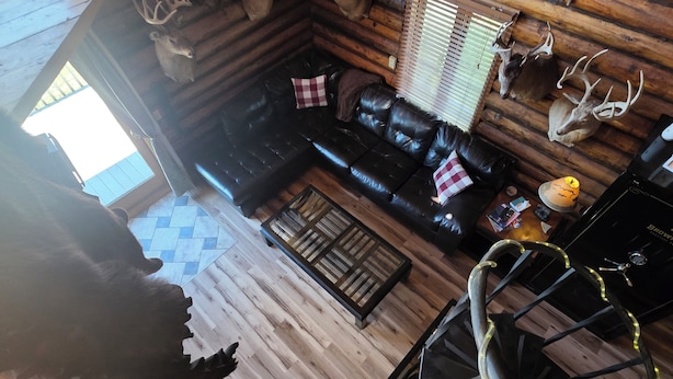 L’intérieur d’un chalet avec un plancher en bois, un canapé en cuir noir, une table à manger et des têtes de cerf fixées au mur.
