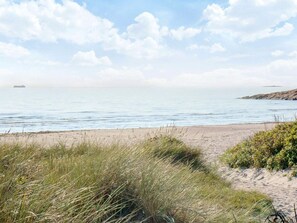 Una spiaggia con un litorale sabbioso, dune erbose e un mare calmo.