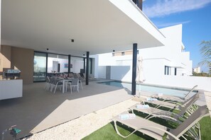 A modern outdoor pool area with lounge chairs, a dining table, and a pool. - Protaras Aqua Pearl Villa Aq12 (Paralimni)