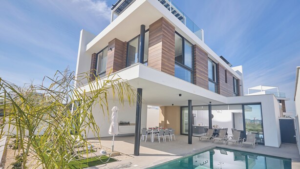 A modern two-story house with a swimming pool, outdoor dining area, and large windows.