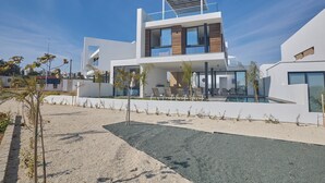 A modern two-story house with a pool, outdoor seating, and a clear sky.