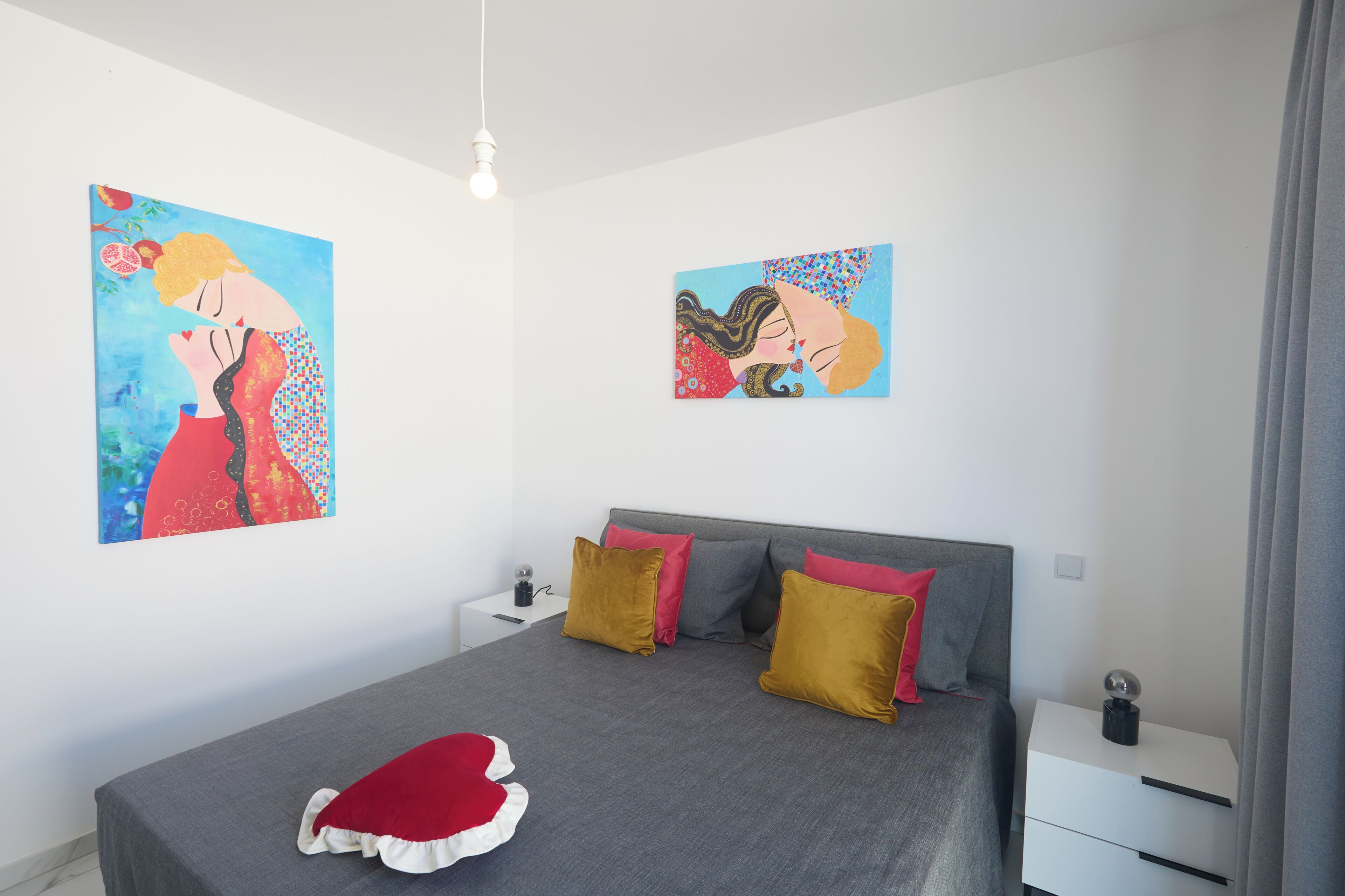 A modern bedroom with a large bed, two nightstands, and two wall-mounted paintings.