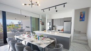 A modern kitchen with a central island, dining area with grey chairs, and a view of the outdoors.