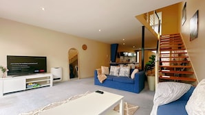 A modern living room with a TV, sofa, coffee table, and a staircase. - City Center Stay, With Parking (Hobart)