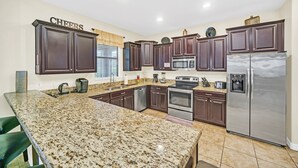 A kitchen with granite countertops, dark wooden cabinets, stainless steel appliances, and a 'CHEERS' sign on the wall.