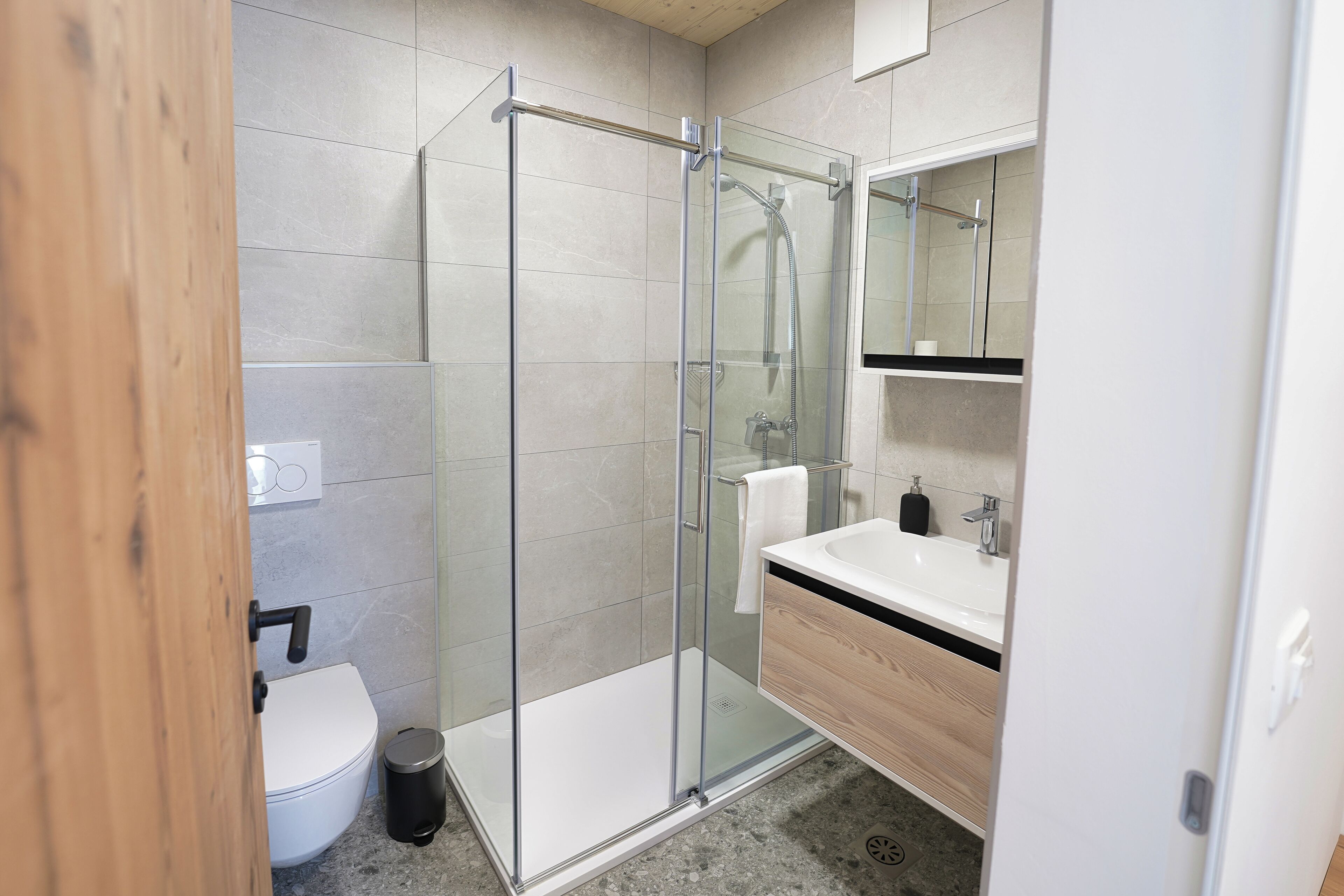 A modern bathroom with a glass-enclosed shower, a white sink, and a wooden vanity.