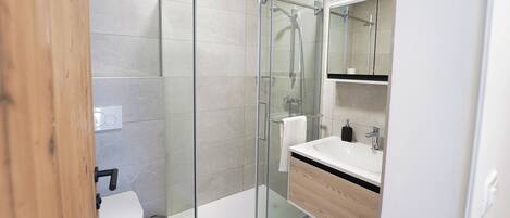 A modern bathroom with a glass-enclosed shower, a white sink, and a wooden vanity.
