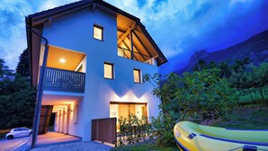 Ein zweistöckiges Haus mit Balkon und sichtbarer Treppe, im Vordergrund ein gelbes Luftboot.