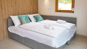 Ein Doppelbett mit weißen Leinen und dekorativen Kissen, eine Holzvertäfelung, ein Fenster mit Blick ins Grüne und eine wandmontierte Leuchte.