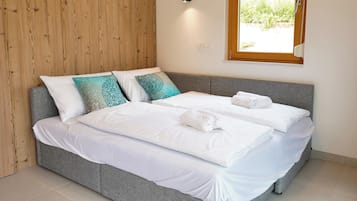 Ein Doppelbett mit weißen Leinen und dekorativen Kissen, eine Holzvertäfelung, ein Fenster mit Blick ins Grüne und eine wandmontierte Leuchte.