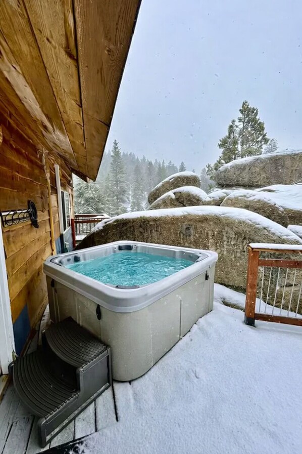 A hot tub on a snowy deck with a wooden cabin in the background.