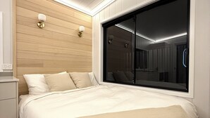 A modern bedroom with a large bed, built-in wooden panel wall, and a sliding glass door leading to a bathroom.