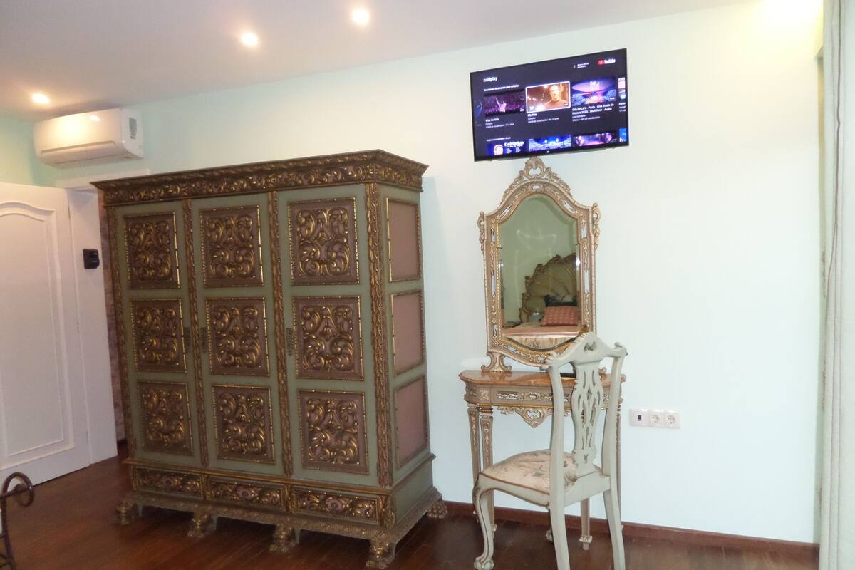 Une pièce comprenant un grand meuble orné, une petite chaise et un téléviseur fixé au mur diffusant un service de streaming.