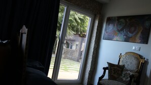 Ein Zimmer mit Bett, einem Sessel, einem Gemälde und Blick durch eine Glastür.