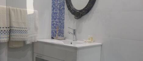 A bathroom with a white vanity, a blue-tiled column, a mirror, a toilet, and patterned floor tiles.