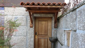 Ein Steinhaus mit Holztür, kleinem Fenster und schmiedeeisernem Zaun.